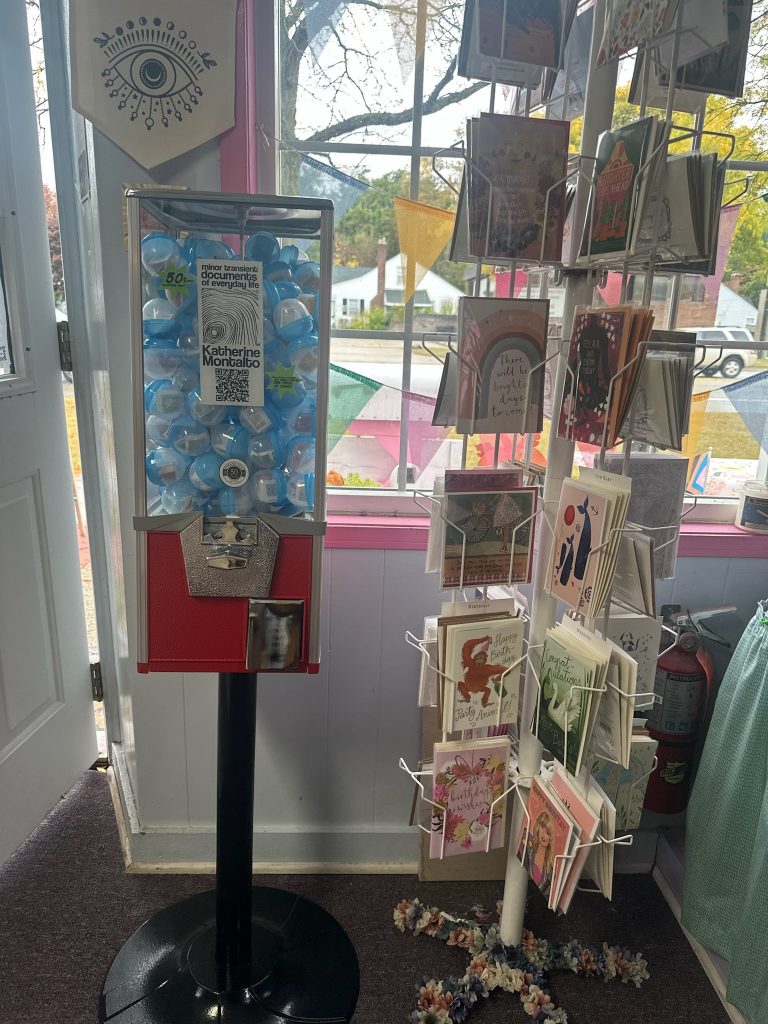 toy capsule machine with a black and white abstract illustration inside that reads minor transient documents of everyday life Katherine Montalto and a QR code that leads to a link to the purchase the book. There are two burst shapes on either side; one reads 50 cents each quarters only. the other reads, each capsule contains one haiku poem and one piece of candy